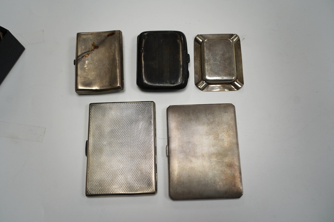 A George VI engine turned silver cigarette case, with yellow metal band, London, 1938, 11.4cm, four other silver cigarette cases and a silver ashtray, gross weight 16.8oz. Condition - poor to fair